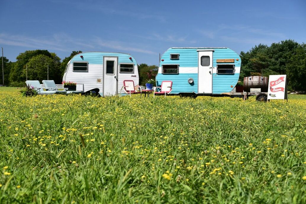 Both of The Little Detour photo booth campers sitting next to each other in a farm field. To the left is a 13' Serro Scotty camper and ti the right is our 13 foot Frolic camper
